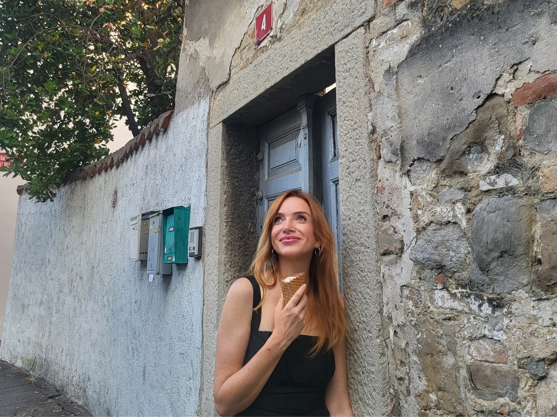 Mojca Mavec stoji pred vrati s kamnitimi oboki, v rokah drži sladoled